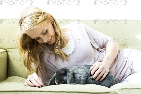 Young woman lying on sofa stroking rabbit