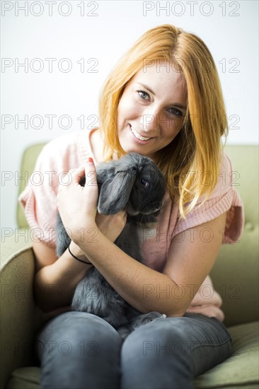 Woman sitting on sofa embracing rabbit