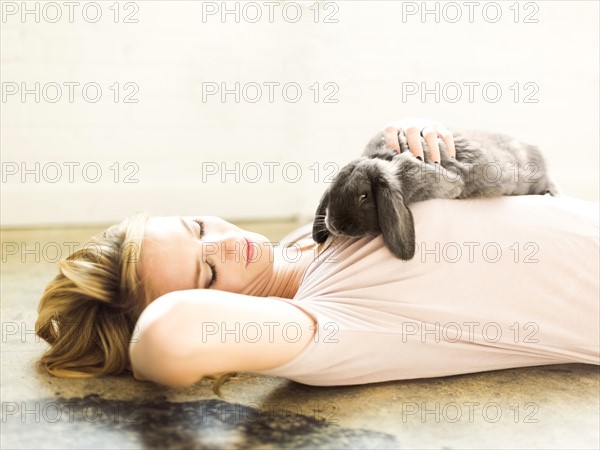 Young woman lying on floor and stroking rabbit