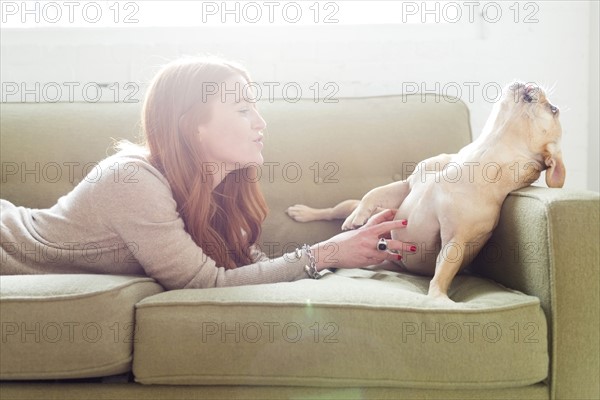 Woman lying on sofa stroking pug