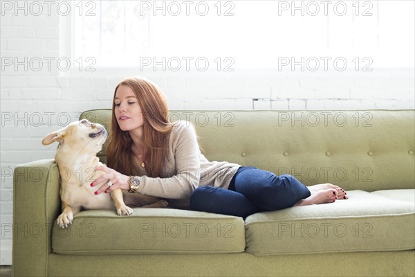 Woman lying on sofa stroking pug