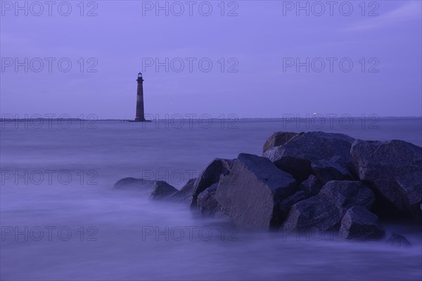 Coastal rocks and lighthouse silhouetted as dusk