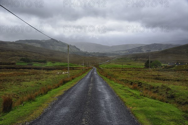 Landscape with asphalt road and green grass, clouds in sky, hills in background