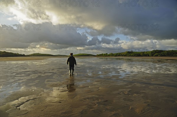 Rear view of man standing water in rubber boots, clouds in sky