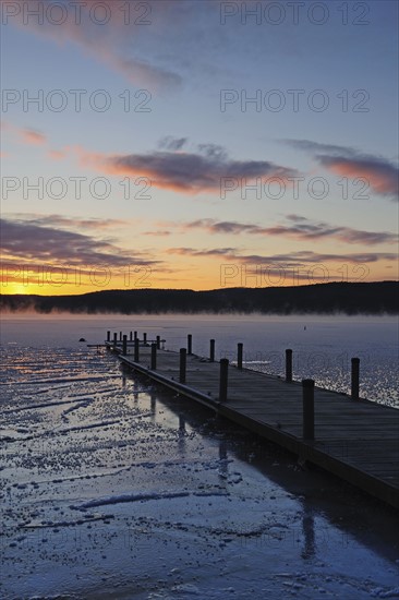 Jetty on frozen lake, hills in background at sunrise