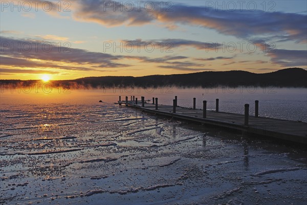 Jetty on frozen lake, hills in background at sunrise