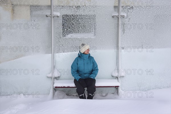 Middle aged woman sitting in bus stop, winter snow