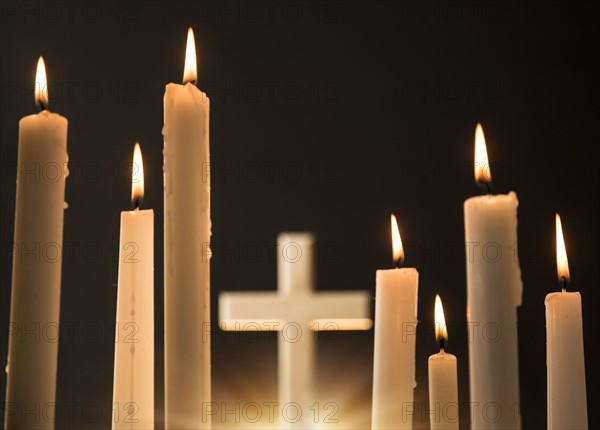 Burning candles with cross in background.