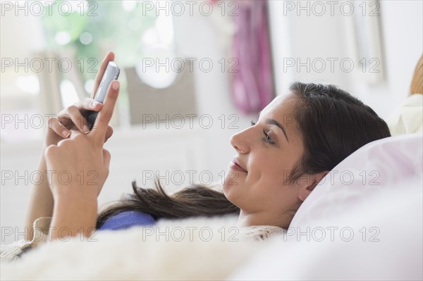 Teenage girl (14-15) texting in bedroom.