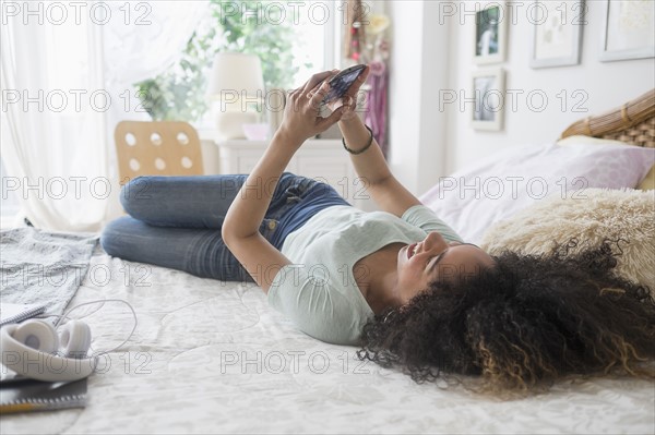 Teenage girl (16-17) texting in bedroom.