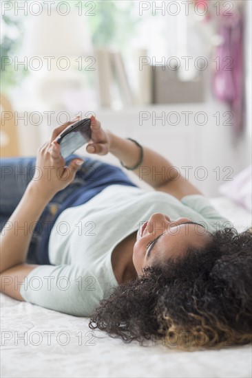 Teenage girl (16-17) texting in bedroom.