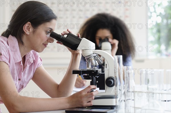 Teenage girls (14-15, 16-17) using microscope in science class.