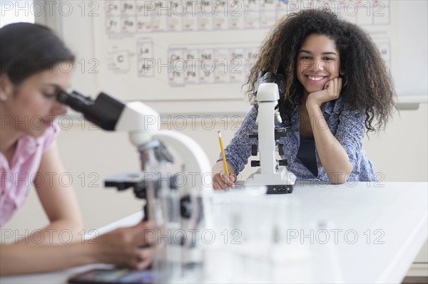 Teenage girls (14-15, 16-17) using microscope in science class.
