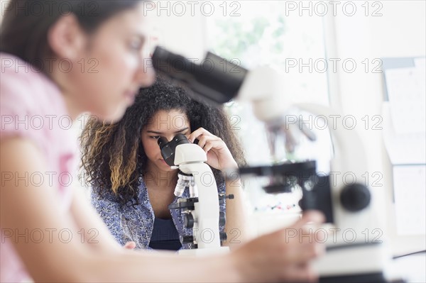 Teenage girls (14-15, 16-17) using microscope in science class.