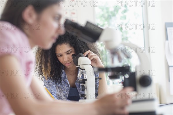 Teenage girls (14-15, 16-17) using microscope in science class.