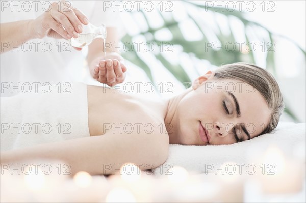 Therapist putting massaging oil on young woman in spa.