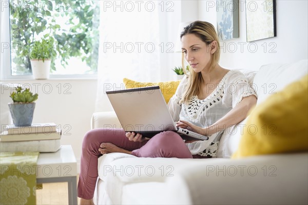 Woman with laptop sitting on sofa .