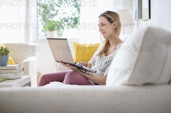 Woman with laptop sitting on sofa .