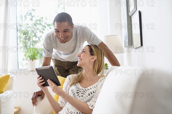 Mid adult couple looking at digital tablet in living room.