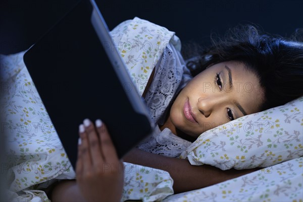 Young woman lying in bed, using digital tablet.