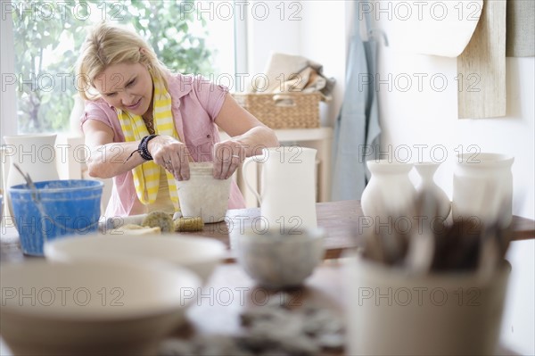 Mature woman making pottery in studio.