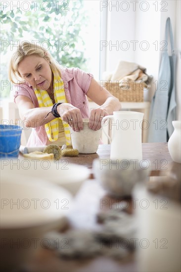 Mature woman making pottery in studio.