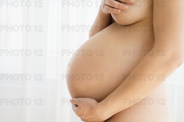 Naked pregnant woman embracing herself