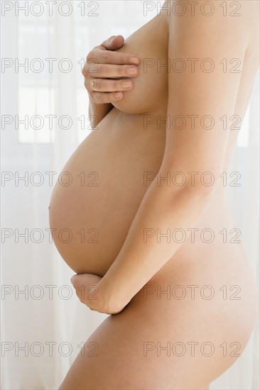 Naked pregnant woman embracing herself