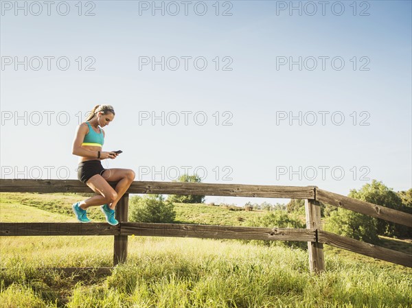 Woman sitting on fence, using smart phone