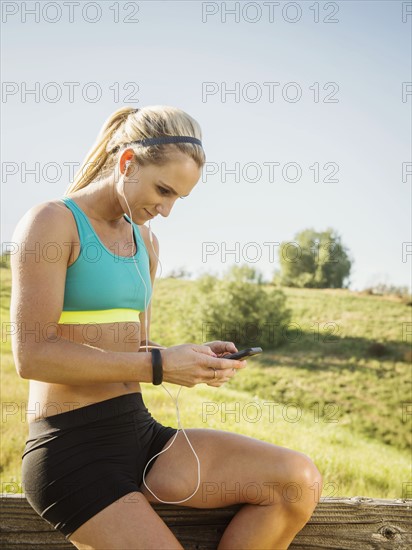 Woman sitting on fence, using smart phone