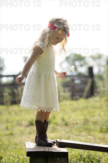 Cute girl (4-5) in white dress standing on fence in meadow