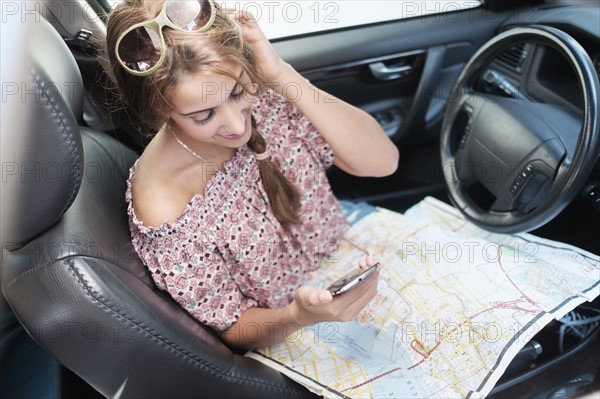 Woman checking phone in car with map on lap.