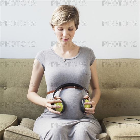 Pregnant woman holding headphones on abdomen