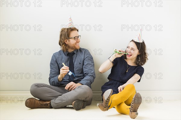 Couple with party horn blowers and party hats sitting on floor