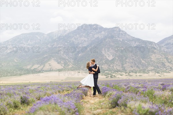 Newlywed couple kissing in lavender field with mountains on background