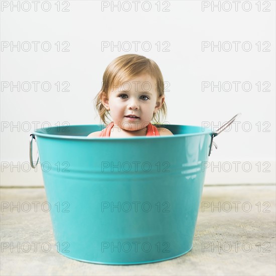 Little girl (2-3) sitting in turquoise bucket