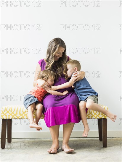 Children (2-3) hugging pregnant mother on bench