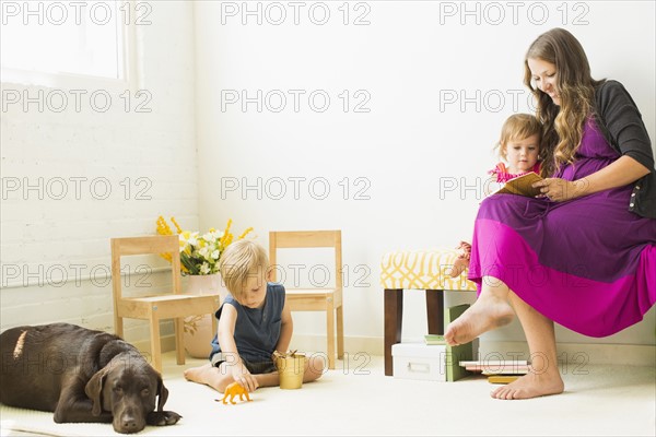 Mother reading to daughter (2-3) while son (2-3) playing on carpet