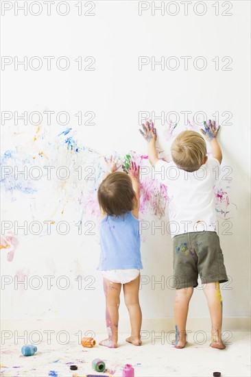 Children (2-3) painting on wall, rear view