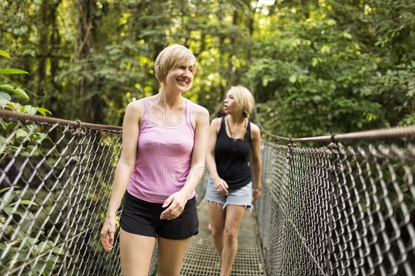 Young women walking on footbridge in forest