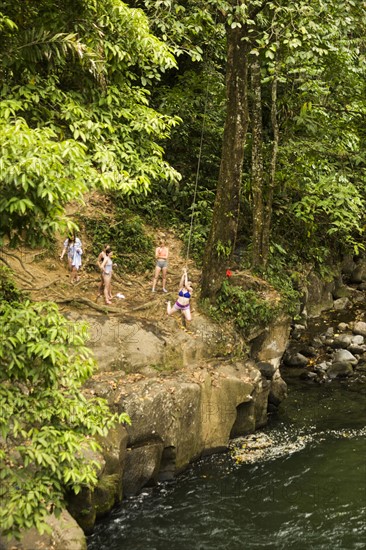 Women swinging on rope swing above river in distance