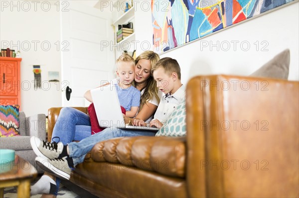 Mother with children (4-5, 6-7) using laptop on sofa