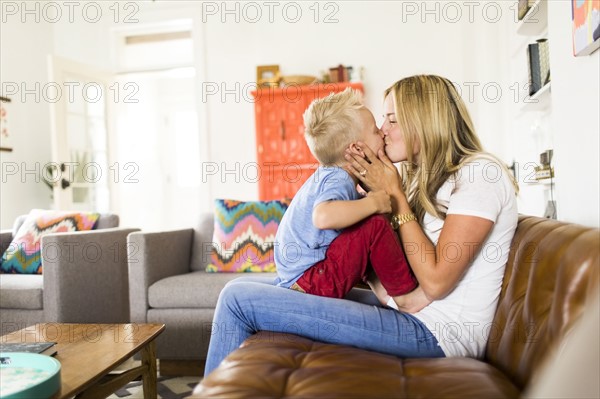 Mother kissing son (4-5) on sofa