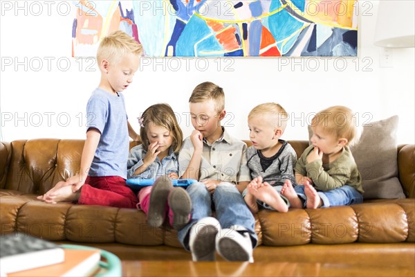 Children (2-3, 4-5, 6-7) sitting on sofa and using digital tablet