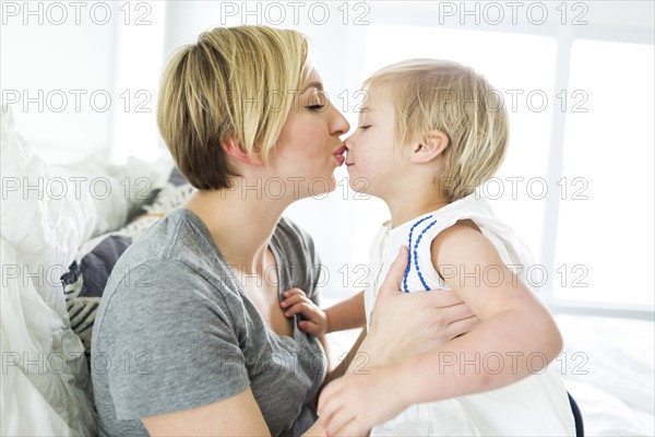Woman kissing girl (2-3) in bedroom