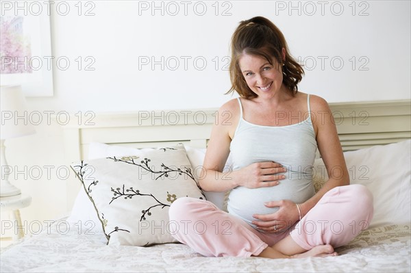 Smiling pregnant woman sitting on bed.