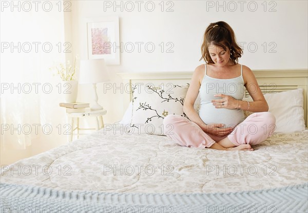 Smiling pregnant woman sitting on bed.