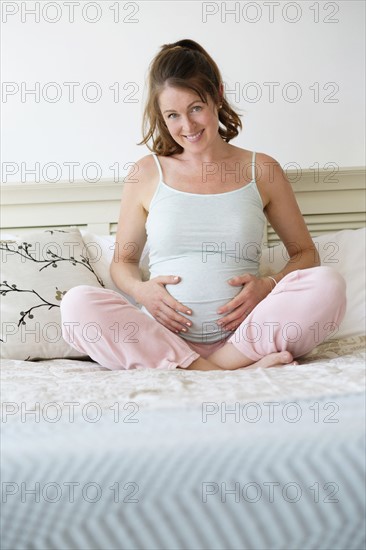 Smiling pregnant woman sitting on bed.