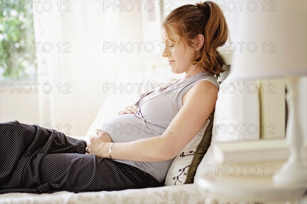 Smiling pregnant woman sitting on bed.