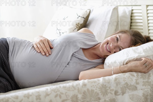 Smiling pregnant woman lying on bed.